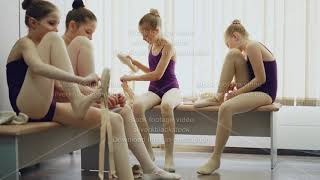 Cheerful kids ballet dancers putting on pointeshoes and talking sitting on benches in light [upl. by Nithsa]